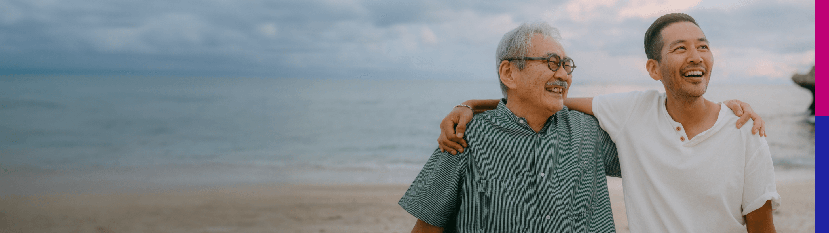 Photo of a younger man hugging an older man near the ocean