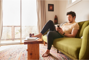 Photo of a man looking down at his phone sitting on a couch